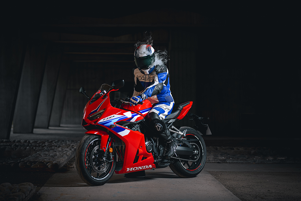 Séance photo pilote moto rouge Honda CBR 650R combinaison cuir bleu et blanche. Casque moto Honda avec fumée qui sort du casque. Photo prise par Alexandre Escudero Photographe Grenoble à l'UGA Grenoble.