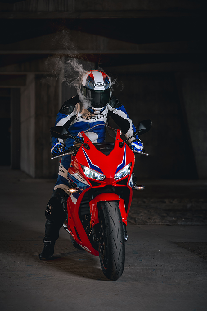 Séance photo pilote moto rouge Honda CBR 650R combinaison cuir bleu et blanche. Casque moto Honda avec fumée qui sort du casque. Photo prise par Alexandre Escudero Photographe Grenoble à l'UGA Grenoble.